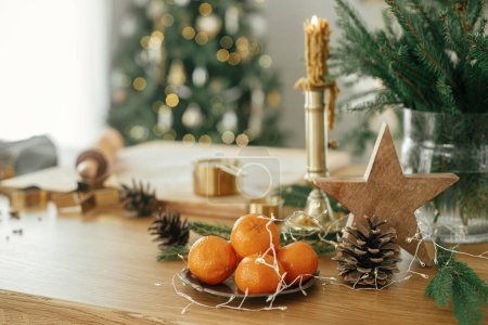 Téléchargez les photos : Je fais des biscuits au pain d'épice de Noël. Étoile en bois, oranges, coupe-métal doré, épices de cuisine et décorations festives sur table rustique contre l'arbre de Noël décoré élégant - en image libre de droit