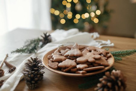 Photo for Delicious gingerbread cookies in wooden plate on rustic table against stylish christmas tree lights bokeh. Fresh baked christmas gingerbread cookies, atmospheric holiday time - Royalty Free Image