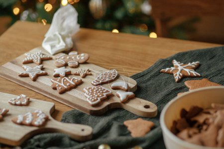 Photo for Gingerbread cookies with icing on rustic wooden table with christmas golden lights. Atmospheric Christmas holiday traditions, family time. Decorating cookies with sugar frosting - Royalty Free Image