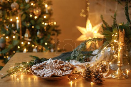Foto de Galletas de jengibre de Navidad con glaseado en plato sobre una mesa rústica festiva con decoraciones contra la iluminación dorada. ¡Feliz Navidad! Deliciosas galletas de jengibre, víspera de las vacaciones atmosféricas - Imagen libre de derechos