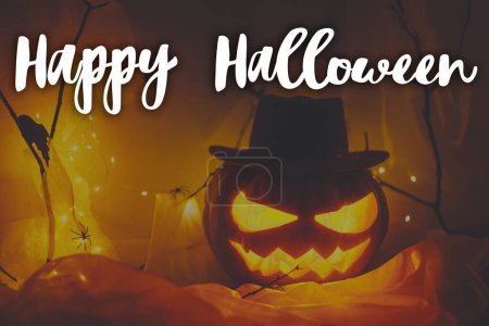 Photo for Happy Halloween! Happy Halloween text and Jack o lantern carved pumpkin with spider web and glowing lights in dark. Spooky atmospheric halloween greeting card, handwritten sign - Royalty Free Image