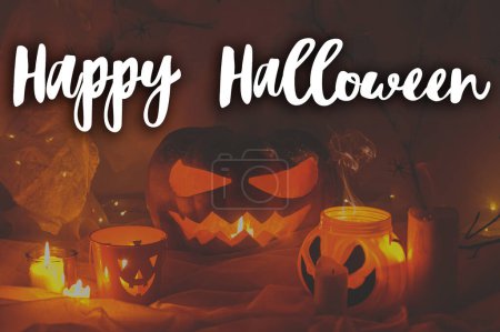 Photo for Happy Halloween! Happy Halloween text and spooky Jack o lantern pumpkin, spider web, candy bucket and glowing lights in dark. Scary atmospheric halloween greeting card, handwritten sign - Royalty Free Image