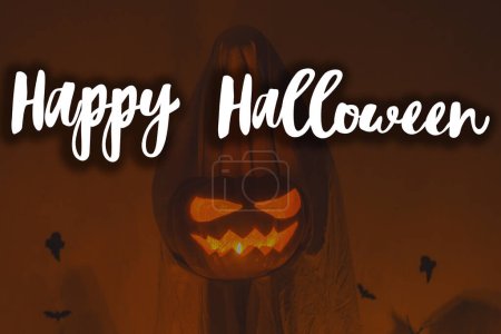 Téléchargez les photos : Joyeux Halloween ! Joyeux texte d'Halloween et fantôme effrayant tenant Jack o lanterne avec une lumière éclatante dans l'obscurité. Carte de vœux fantasmagorique d'Halloween atmosphérique, panneau manuscrit - en image libre de droit