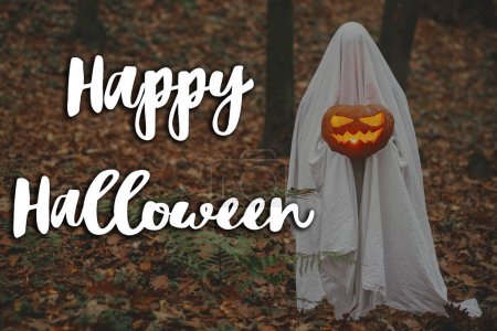 Photo for Happy Halloween! Happy Halloween text and spooky ghost holding glowing jack o lantern in moody dark autumn forest. Scary atmospheric halloween greeting card, handwritten sign - Royalty Free Image