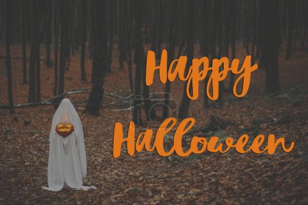 Téléchargez les photos : Joyeux Halloween ! Joyeux texte d'Halloween et fantôme effrayant tenant Jack o lanterne rougeoyante dans la forêt d'automne sombre et humide. Carte de voeux halloween atmosphérique effrayante, panneau manuscrit - en image libre de droit