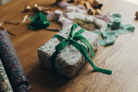 Foto de Envolver regalos de Navidad. Elegante regalo, papel de regalo festivo, cintas, tijeras, estrellas y campanas de latón en la mesa de madera. Vacaciones de invierno atmosféricas - Imagen libre de derechos