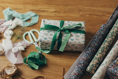 Téléchargez les photos : Cadeau de Noël élégant, papier d'emballage festif, rubans, ciseaux, ornements vintage et cloches en laiton sur une table en bois. Emballage cadeau de Noël. Joyeux Noël ! Préparation des vacances d'hiver - en image libre de droit