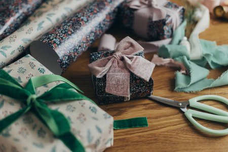 Téléchargez les photos : Emballage cadeaux de Noël. Élégant cadeau, papier d'emballage festif, rubans, ciseaux, ornements vintage et cloches en laiton sur table en bois. Préparation aux vacances d'hiver atmosphériques - en image libre de droit