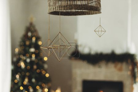 Téléchargez les photos : Décorer la maison avec des araignées de paille de Noël. Décoration rustique nordique en paille suspendue sur fond de lumières dorées festives bokeh dans le salon moderne de la ferme. Traditions de vacances - en image libre de droit