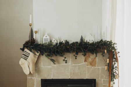 Photo for Rustic christmas fireplace with warm knitted stockings and stylish decoration on fir branches. Cozy stockings hanging on mantel in modern farmhouse living room. Atmospheric winter holiday - Royalty Free Image