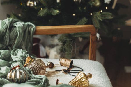 Foto de Adornos de Navidad estética. Elegantes adornos de Navidad vintage, cintas, campanas de latón y tijeras en la silla blanca acogedor. ¡Feliz Navidad! Decoración para el concepto de vacaciones de Navidad - Imagen libre de derechos