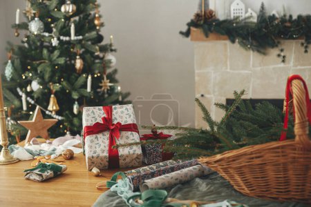 Téléchargez les photos : Cadeaux de Noël élégants et décorations festives sur la table sur fond de beau sapin de Noël vintage et cheminée. Joyeux Noël et Joyeuses Fêtes ! Préparation des vacances d'hiver - en image libre de droit