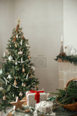 Foto de Elegantes regalos de Navidad envueltos, cesta rústica con ramas de abeto y decoraciones modernas en la mesa en la habitación escandinava decorada festiva. Feliz Navidad y Felices Fiestas! - Imagen libre de derechos