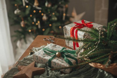 Foto de Feliz Navidad y Felices Fiestas! Elegantes regalos de Navidad envueltos, cesta rústica con ramas de abeto y decoraciones modernas en la mesa de cerca. Imagen escandinava atmosférica - Imagen libre de derechos