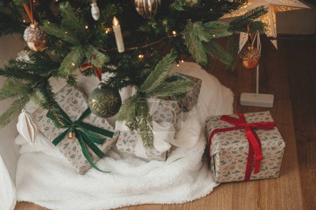 Foto de Elegantes regalos de Navidad envueltos y cesta rústica con ramas de abeto bajo el árbol de Navidad decorado festivo en la habitación escandinava. Feliz Navidad y Felices Fiestas! - Imagen libre de derechos