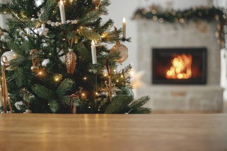 Foto de Elegante mesa de madera contra el árbol de Navidad con luces y chimenea. Plantilla festiva de Navidad y tablero de madera se burlan de producto. Fondo de Navidad, espacio de copia - Imagen libre de derechos