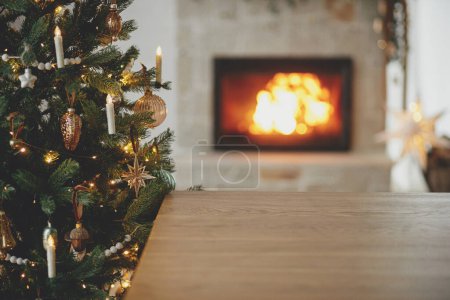 Téléchargez les photos : Table en bois élégant contre l'arbre de Noël avec des lumières et cheminée en feu. Modèle de fête de Noël et planche en bois maquettes pour le produit. Fond de Noël, espace de copie - en image libre de droit
