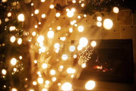 Téléchargez les photos : Atmosphérique magique veille de Noël à la cheminée. Élégant arbre de Noël illuminé sur fond de lumières dorées bokeh et cheminée en feu dans la salle du soir. Joyeux Noël! - en image libre de droit