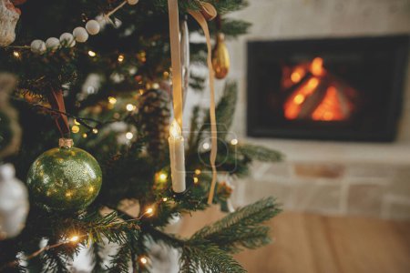 Téléchargez les photos : Des boules de Noël élégantes sur un arbre se ferment contre une cheminée en feu. Bel arbre de Noël décoré avec des boules vintage et des rubans. Ambiance de Noël. Joyeux Noël! - en image libre de droit
