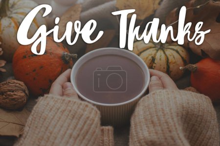 Photo for Happy Thanksgiving! Give thanks text and hands in sweater holding warm cup of tea with stylish pumpkins and fall leaves. Season Greeting card, handwritten sign - Royalty Free Image