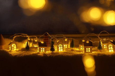 Téléchargez les photos : Confortable village miniature de Noël. Élégantes petites maisons lumineuses et des arbres de Noël sur une couverture de neige molle avec des lumières bokeh en soirée. Village d'hiver atmosphérique nature morte. Joyeux Noël! - en image libre de droit