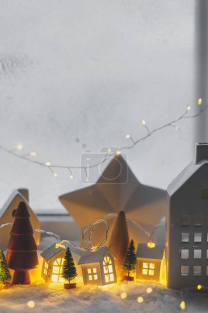 Foto de Aldea invernal en miniatura atmosférica. Pequeñas casas de cerámica con estilo y árboles de madera de Navidad en la manta de nieve con luces brillantes en la noche. Fondo moderno de Navidad. Felices Fiestas! - Imagen libre de derechos