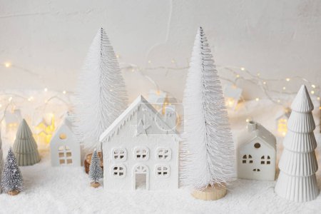 Photo for Atmospheric miniature white christmas village. Stylish little christmas houses and trees on snow blanket with glowing lights. Christmas modern winter village, holiday banner. Happy Holidays! - Royalty Free Image