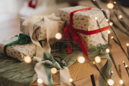 Foto de Elegantes regalos de Navidad envueltos con cintas y tijeras en la mesa con luces doradas festivas. Feliz Navidad y Felices Fiestas! Regalos modernos, víspera de Navidad atmosférica - Imagen libre de derechos
