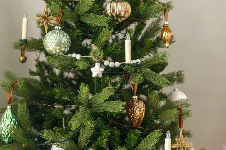 Téléchargez les photos : Élégant arbre de Noël décoré avec des boules d'or vintage et des bougies. Atmospheric winter holidays preparation. Ornements de Noël modernes suspendus sur les branches gros plan - en image libre de droit