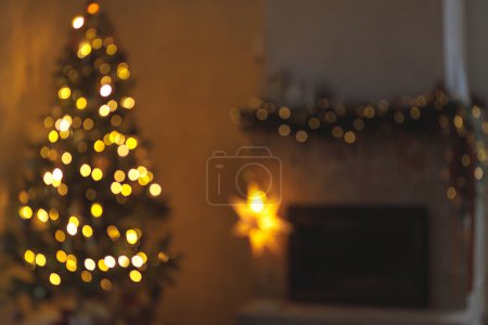Téléchargez les photos : Fond de Noël bokeh doré. Veille de Noël atmosphérique à la cheminée. Image floue de l'arbre de Noël illuminé et cheminée décorée festive avec des lumières dans la salle scandinave du soir - en image libre de droit