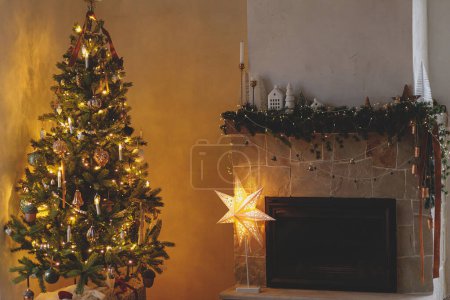 Photo for Stylish christmas living room with modern decorated christmas tree and festive decor on fireplace mantel with golden light. Atmospheric christmas eve in scandinavian room. Happy Holidays! - Royalty Free Image