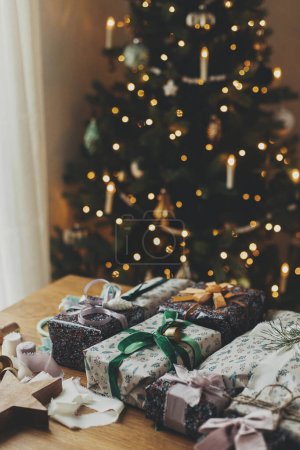 Foto de ¡Feliz Navidad! Envolviendo regalo de Navidad. Elegante regalo de Navidad, papel de regalo festivo, cintas, tijeras, adornos vintage y campanas de latón en la mesa de madera. Preparación de vacaciones de invierno - Imagen libre de derechos