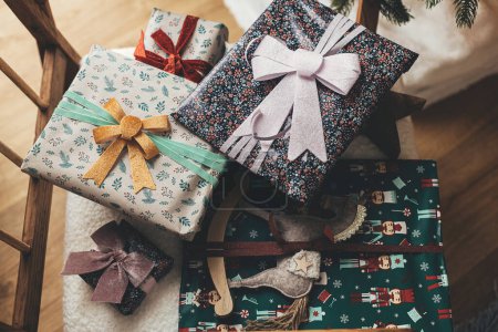 Téléchargez les photos : Joyeux Noël ! Cadeaux de Noël élégants enveloppés dans du papier de fête avec des arcs, des jouets vintage sur la vue de dessus de chaise moderne. Vacances d'hiver dans l'atmosphère, cadeau vintage moderne - en image libre de droit