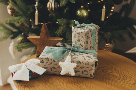 Téléchargez les photos : Cadeaux de Noël élégants en papier d'emballage festif avec arcs, ornements vintage, jouet sur table en bois sur fond de lumières d'arbre de Noël. Joyeuses fêtes ! Veille de Noël atmosphérique - en image libre de droit