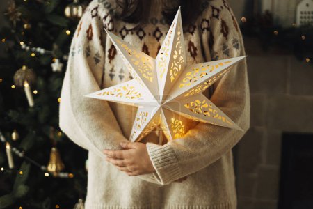 Photo for Stylish glowing big christmas star in hands of on background of decorated christmas tree with vintage baubles and lights. Merry Christmas! Atmospheric magic winter time - Royalty Free Image