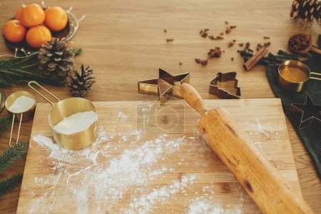 Téléchargez les photos : Je fais des biscuits au pain d'épice de Noël. Farine sur planche de bois, rouleau à pâtisserie, coupe-métal doré, épices de cuisine et décorations festives sur table rustique - en image libre de droit