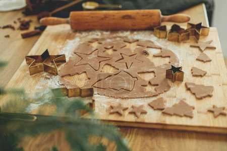 Foto de Masa de pan de jengibre con cortadores de oro, rodillo, especias de cocina y decoraciones festivas en la mesa de madera rústica. Hacer galletas de jengibre de Navidad, tiempo de vacaciones atmosféricas - Imagen libre de derechos