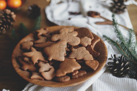 Téléchargez les photos : Biscuits au pain d'épice de Noël dans une assiette en bois sur une table rustique avec branches de sapin, cône de pin, serviette. Joyeux Noël ! Délicieux biscuits au pain d'épice frais en gros plan, vacances atmosphériques - en image libre de droit