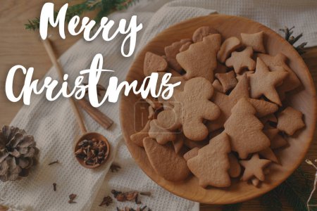 Photo for Merry Christmas text on christmas gingerbread cookies in wooden plate on table flat lay with fir branches, pinecone, spices. Happy Holidays! Season's greeting card. Handwritten sign - Royalty Free Image