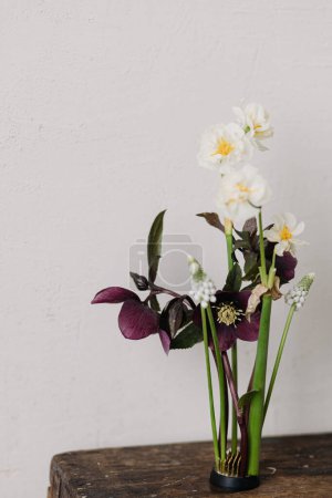 Photo for Spring flowers rustic still life. Beautiful helleborus, muscari and daffodil composition on kenzan on aged wooden background. First spring flowers gardening - Royalty Free Image
