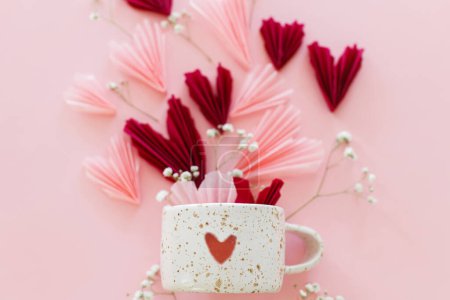 Téléchargez les photos : Joyeuse Saint Valentin ! Coeurs roses et rouges élégants, fleurs et tasse moderne avec coeur plat reposent sur fond rose. Valentines coeurs découpes de papier et tasse. Amour et fête des mères - en image libre de droit