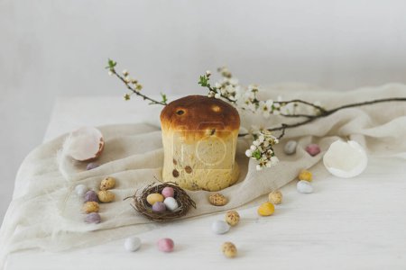 Téléchargez les photos : Joyeux Pâques ! Élégants œufs de Pâques en chocolat dans le nid, fleurs de printemps, pain traditionnel et tissu de lin sur table en bois rustique. Bannière simple moderne de Pâques, espace pour le texte. Salutations saisonnières - en image libre de droit
