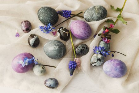 Foto de Elegantes huevos de Pascua, suaves flores de primavera y tela de lino sobre una mesa blanca rústica. Espacio para el texto. ¡Feliz Pascua! Mármol natural pintado y huevos morados. Saludos de temporada - Imagen libre de derechos