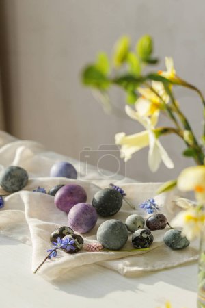 Photo for Stylish easter eggs, gentle spring flowers and linen cloth on rustic white table in sunlight. Space for text. Happy Easter! Natural painted marble and purple eggs. Seasons greetings - Royalty Free Image