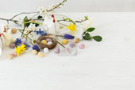 Téléchargez les photos : Joyeux Pâques ! Œufs de Pâques élégants en chocolat dans le nid, fleurs de printemps, figurine de poulet sur table en bois rustique blanc. Bannière simple moderne de Pâques, espace pour le texte. Salutations saisonnières - en image libre de droit