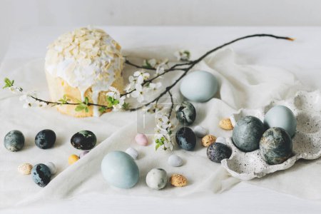 Foto de Elegantes huevos de Pascua, panettone y flores de primavera en tela de lino en la mesa rústica. Huevos de tinte natural y flor de cerezo, bodegón festivo mínimo. Feliz Pascua! - Imagen libre de derechos
