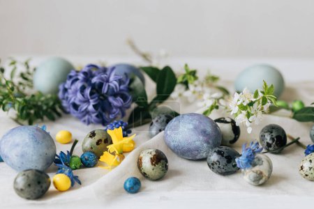 Photo for Stylish easter eggs and spring flowers on rustic wooden table. Happy Easter! Natural dye marble and blue eggs, purple hiacynt blossoms and daffodils. Minimal still life. - Royalty Free Image