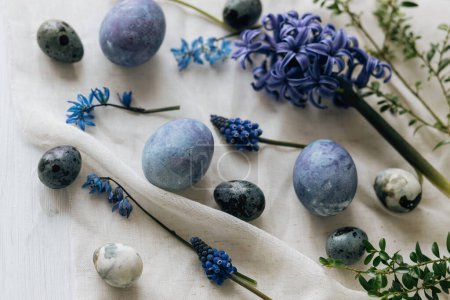 Photo for Stylish easter eggs and spring flowers on rustic wooden table. Happy Easter! Natural dye marble and blue eggs, purple hiacynt blossoms on linen. Minimal flat lay - Royalty Free Image