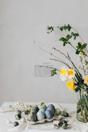 Foto de ¡Feliz Pascua! Elegantes huevos de Pascua y flores de primavera en la mesa rústica de lino. Huevos naturales pintados de mármol azul en bandeja y ramillete de narcisos. Moderno bodegón mínimo - Imagen libre de derechos