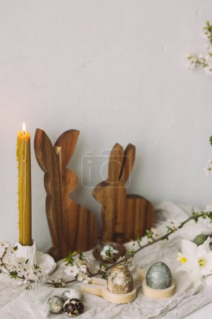 Foto de Elegantes huevos de Pascua, conejos de madera, flor de cerezo y composición de velas en mesa rústica. ¡Feliz Pascua! Modernos huevos de mármol teñido natural y flores de primavera. Naturaleza muerta rural - Imagen libre de derechos